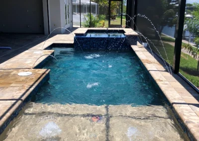 A rectangular pool with water jets, surrounded by a screened enclosure, showcases a recent pool remodel. A hot tub is attached at the far end, offering a seamless blend of relaxation and style. Flamingo Pools, Punta Gorda FL