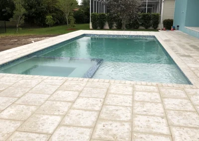 A stunning rectangular swimming pool with an attached hot tub graces the backyard, surrounded by a paved stone deck. This masterpiece is the result of expert pool construction, offering both relaxation and style. Flamingo Pools, Punta Gorda FL